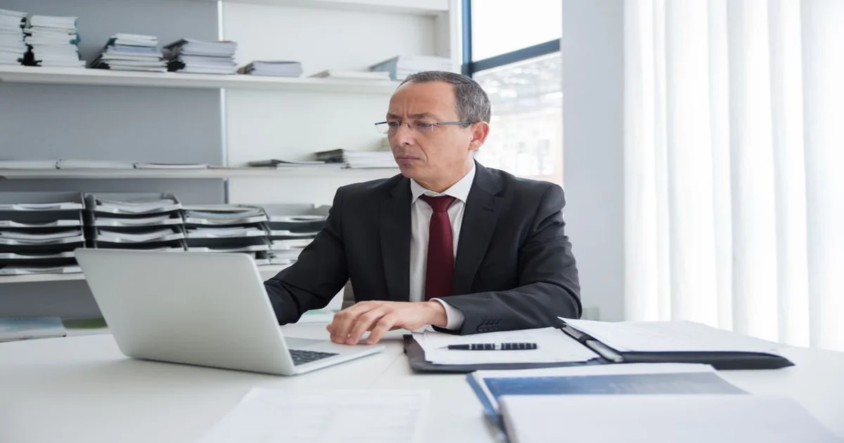Gerente revisando documentos incompletos en su escritorio antes de tomar una decisión, con el equipo trabajando al fondo