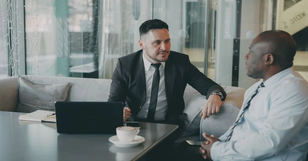Dos personas conversando en una oficina corporativa, una en posición de guía y otra escuchando activamente