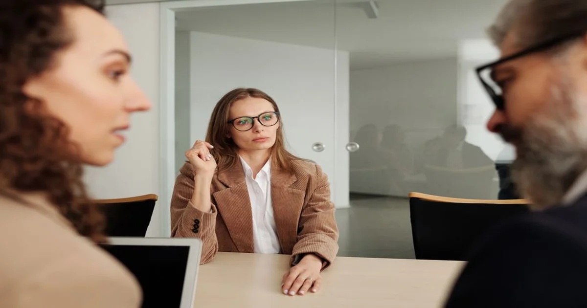 Gerente y colaborador en conversación tensa frente a una mesa de reuniones, expresiones serias pero respetuosas