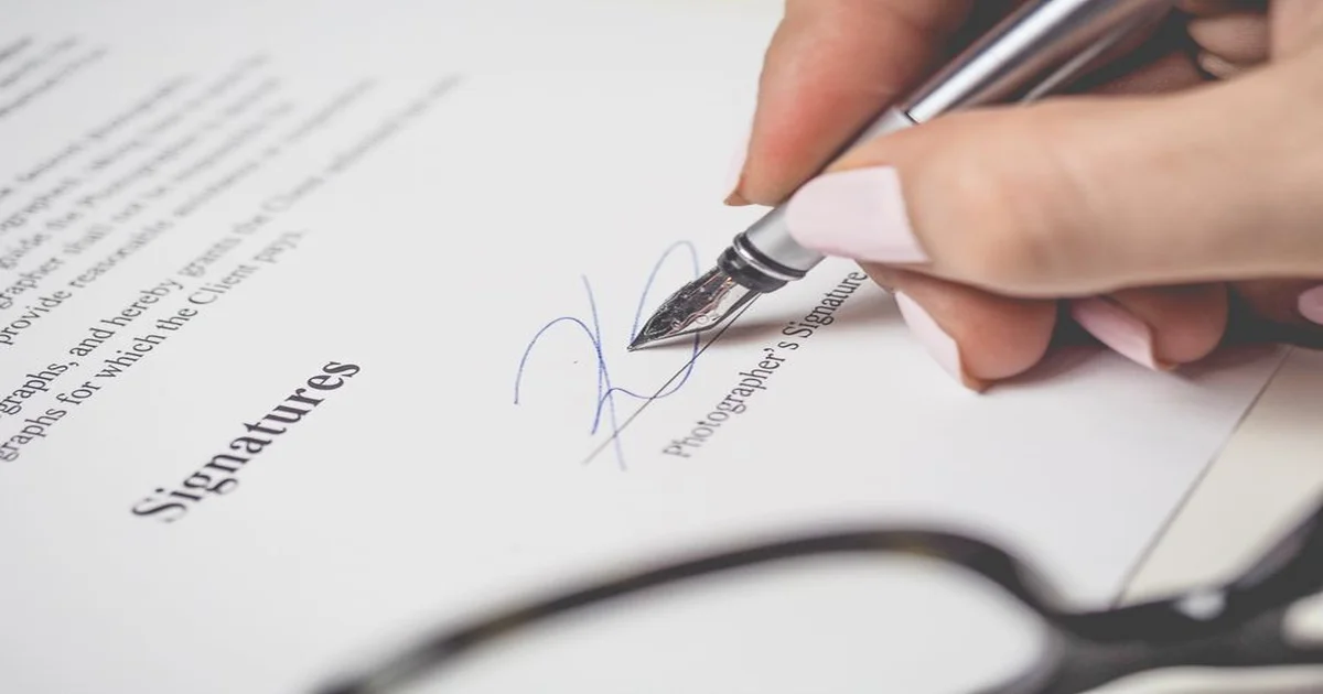 Gerente firmando una carta sobre la mesa, con un icono de IA abierto en la laptop pero difuminado al fondo.
