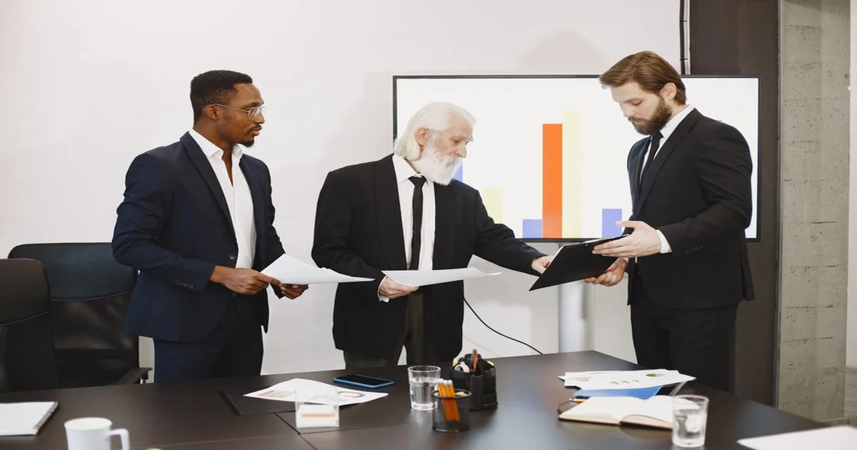 Gerente explicando una tarea a su equipo alrededor de una mesa de trabajo con documentos y pantalla